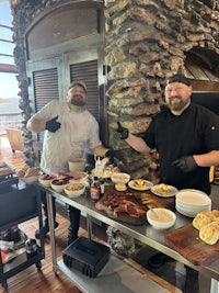 two men standing in front of a table full of food